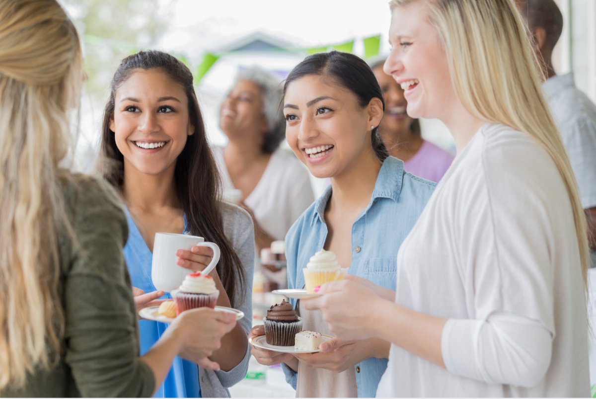 Friends laughing together over cupcakes and coffee at a celebration
