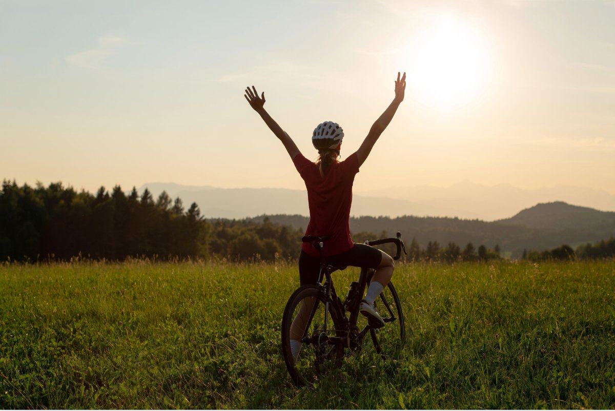 A cyclist raising both arms in triumph on a hilltop at sunset
